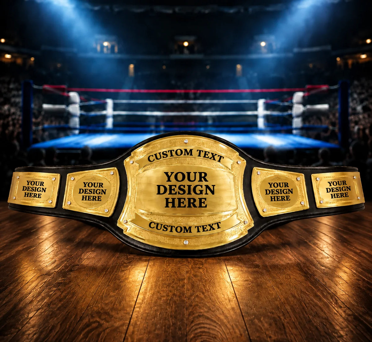A custom wrestling or boxing championship belt with gold plates and black straps, displayed on a wooden floor with a blurred boxing ring and arena in the background.