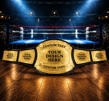 A custom wrestling or boxing championship belt with gold plates and black straps, displayed on a wooden floor with a blurred boxing ring and arena in the background.