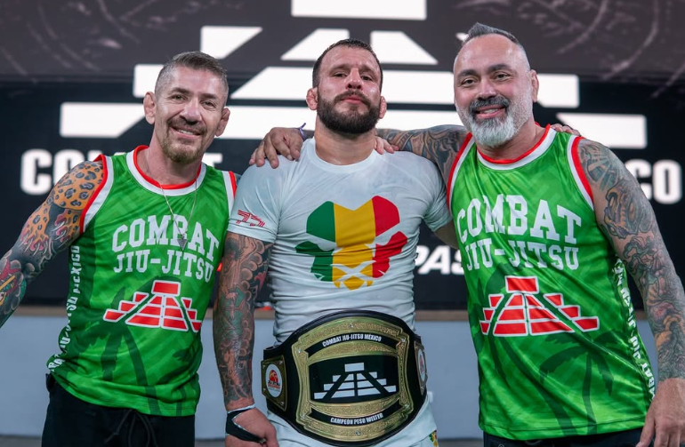 Three men standing together in a studio setting, with the central figure holding a black and gold jiu-jitsu championship belt. The two men on either side wear matching bright green Combat Jiu-Jitsu jerseys with red and white trim, and the center man wears a white T-shirt with a green, yellow, and red graphic.