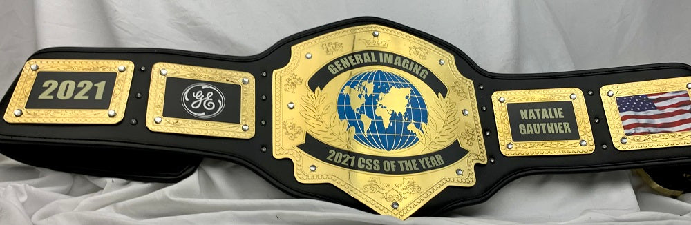 A custom black and gold championship belt plaque for the 2021 CESS of the Year, featuring a central gold globe emblem and nameplates for Natalya Gauthier and General Imaging.