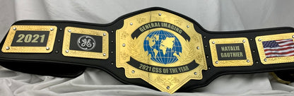 A custom black and gold championship belt plaque for the 2021 CESS of the Year, featuring a central gold globe emblem and nameplates for Natalya Gauthier and General Imaging.