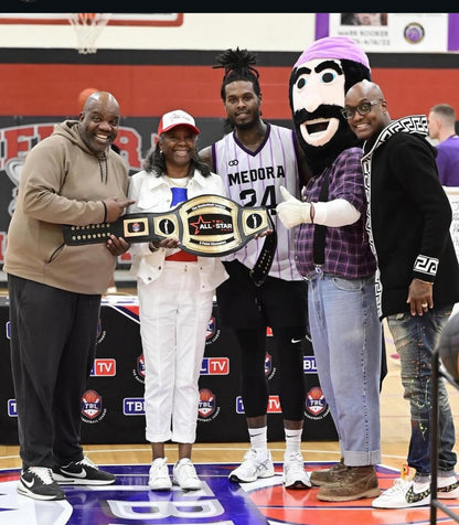 Custom Basketball MVP award title belt on basketball court holding a championship belt. The central figures include a man in a white and purple Medora 24 jersey, a woman in white pants, and others in casual and mascot attire.